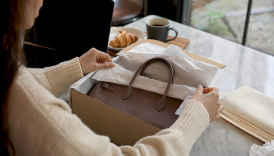 Hands packaging a luxury handbag for return
