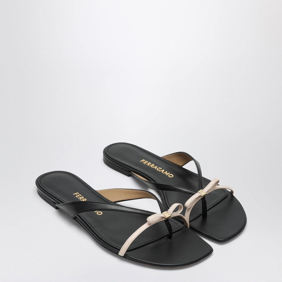 Black sandals with a beige bow on a light gray background