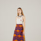 Woman wearing a white Adidas x Gucci  tank top and colorful skirt on a plain background