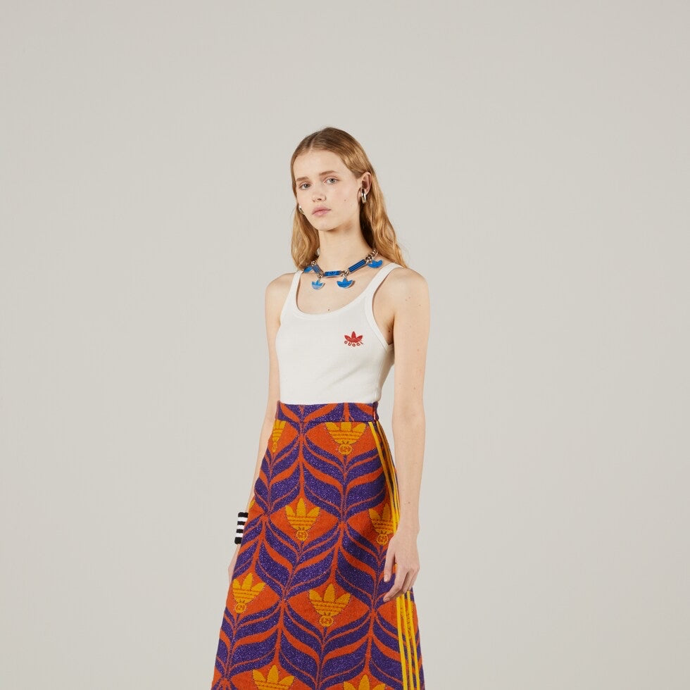 Woman wearing a white Adidas x Gucci  tank top and colorful skirt on a plain background