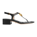 Black sandal with gold buckle on a light gray background