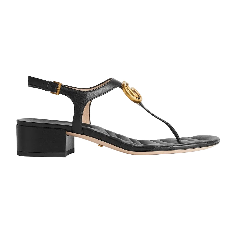 Black sandal with gold buckle on a light gray background