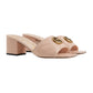 Beige high-heeled sandals with gold logo on a light gray background