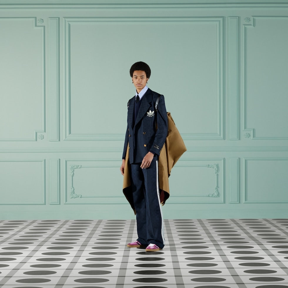 Man in a formal suit with a coat over his shoulder against a light green wall.