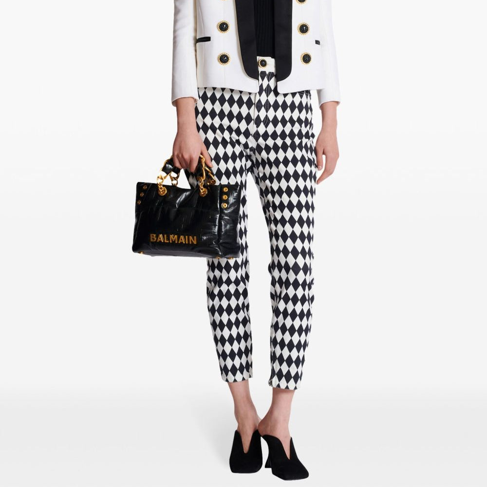 Person wearing a white blazer with gold buttons, black and white checkered pants, and holding a Balmain handbag on a white background.