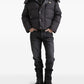 Person wearing a black puffer jacket, black shirt, black jeans, and black boots on a white background
