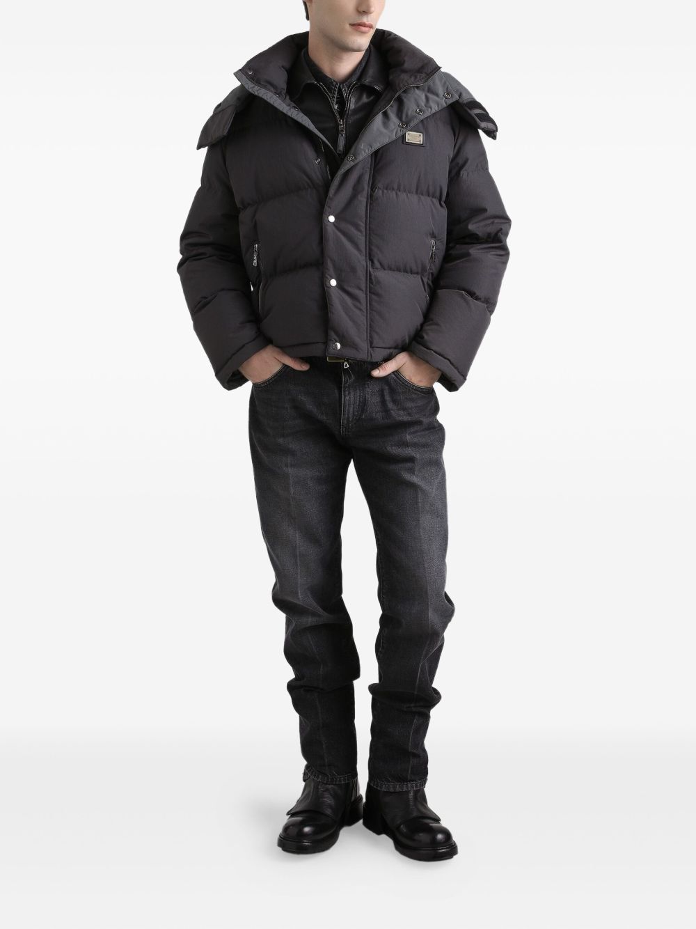 Person wearing a black puffer jacket, black shirt, black jeans, and black boots on a white background