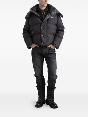 Person wearing a black puffer jacket, black shirt, black jeans, and black boots on a white background