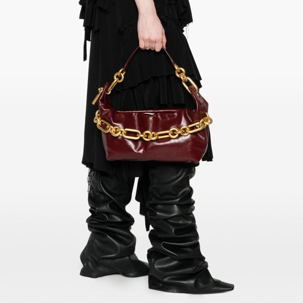 Person holding a burgundy handbag with gold chain detail against a white background