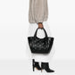 Person holding a black quilted handbag on a white background
