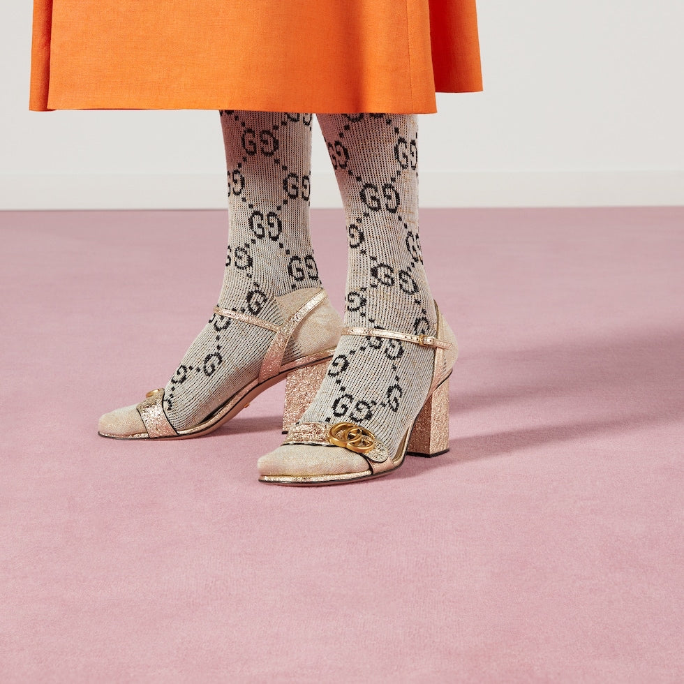 Close-up of high-heeled shoes with a gold chain detail on a pink background