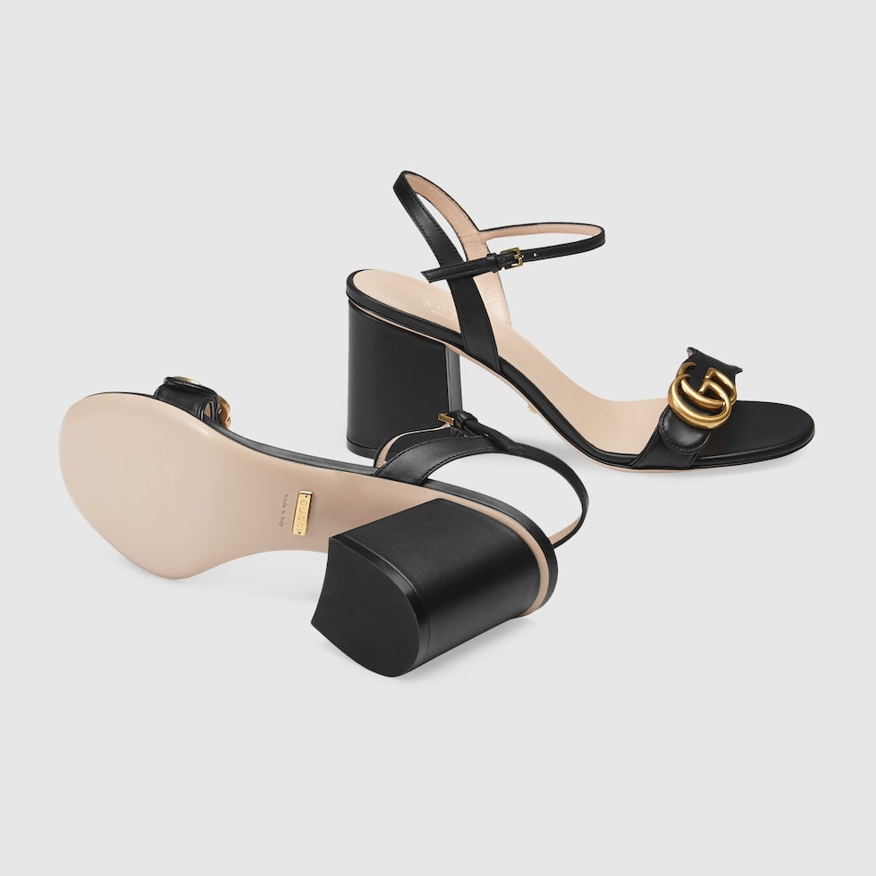 Black high-heeled sandals with a gold logo on a light gray background