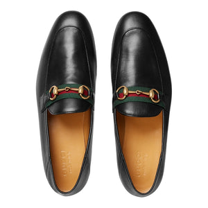 Pair of black Gucci loafers with gold and green accents on a light gray background