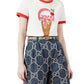Person wearing a white t-shirt with a red ice cream cone design and blue jeans with a Gucci logo.
