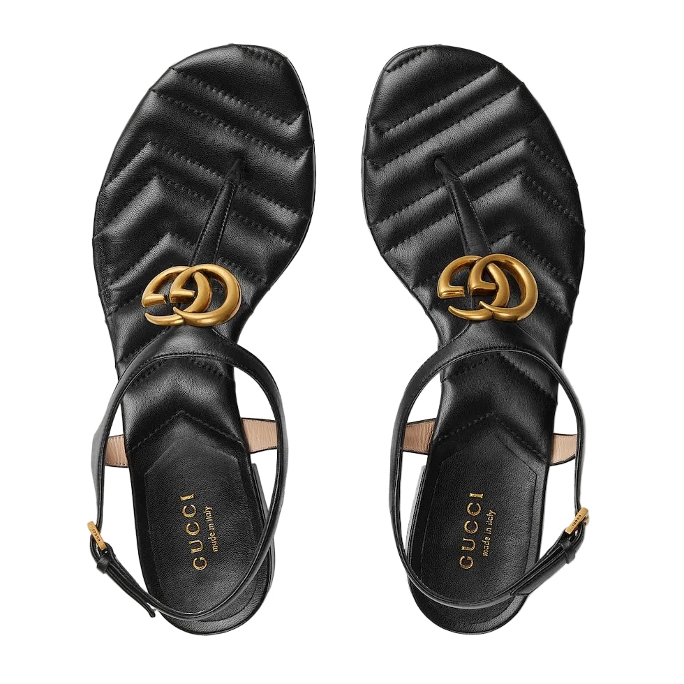 Black Gucci sandals with gold logo on a light gray background