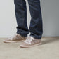 Person wearing blue jeans and beige sneakers with a Gucci logo on a neutral background