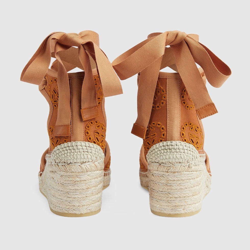Pair of tan wedge sandals with raffia soles on a light gray background