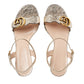 Pair of gold and silver glittery high-heeled sandals with a brand logo on a light gray background
