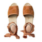 Pair of brown espadrille sandals with decorative straps on a light gray background