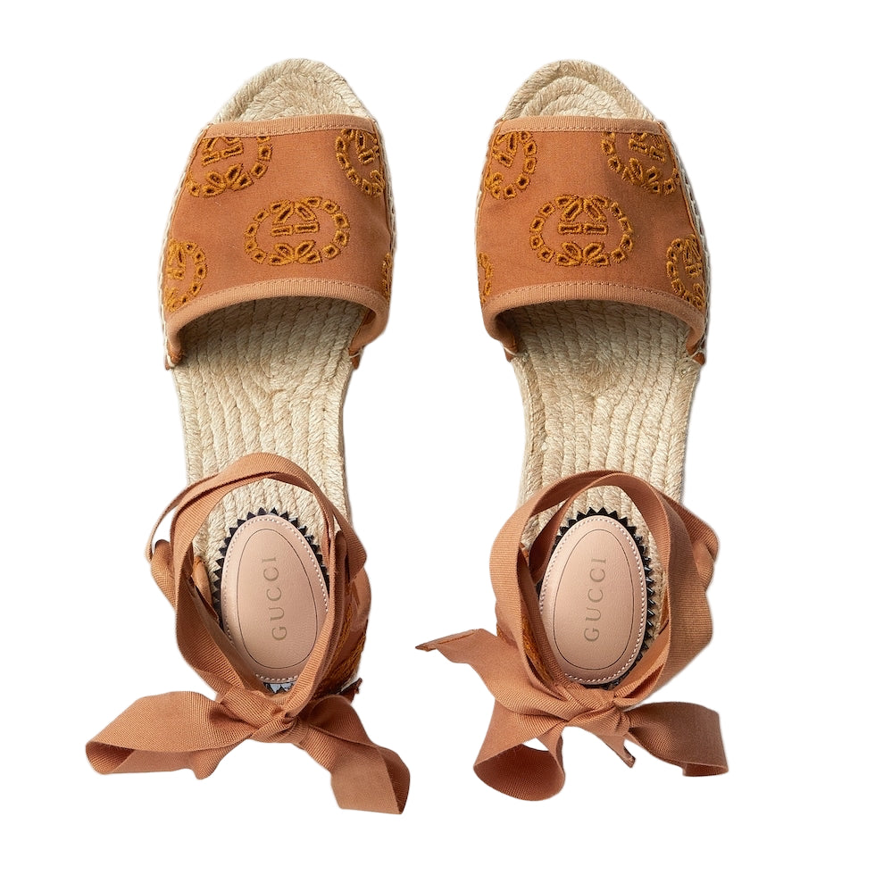Pair of brown espadrille sandals with decorative straps on a light gray background