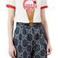 Person wearing a Gucci ice cream-themed t-shirt and GG patterned pants on a white background