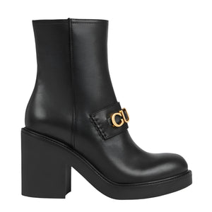 Black ankle boot with gold buckle on a light gray background