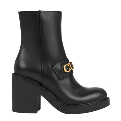 Black ankle boot with gold buckle on a light gray background