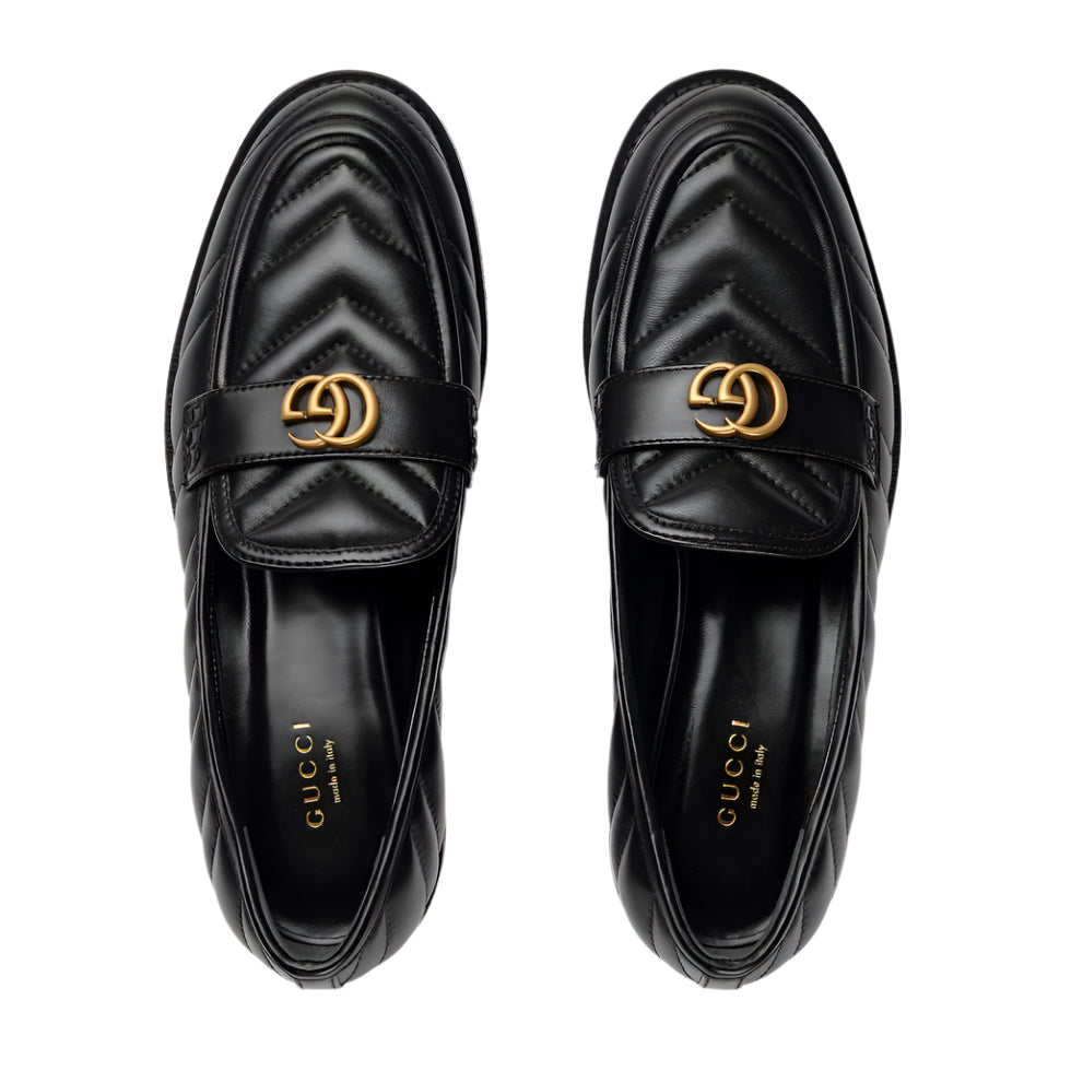 Pair of black Gucci loafers with gold logo on a light gray background