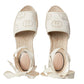 Pair of cream-colored espadrilles with ribbon details on a light gray background