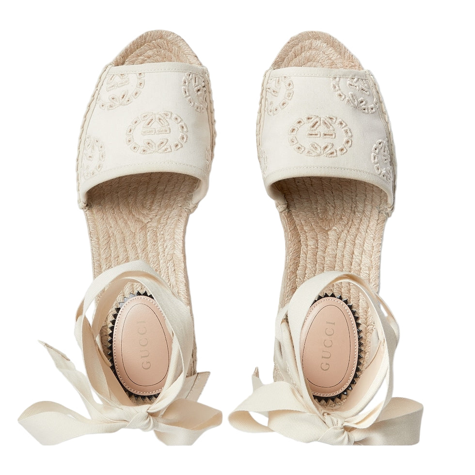 Pair of cream-colored espadrilles with ribbon details on a light gray background