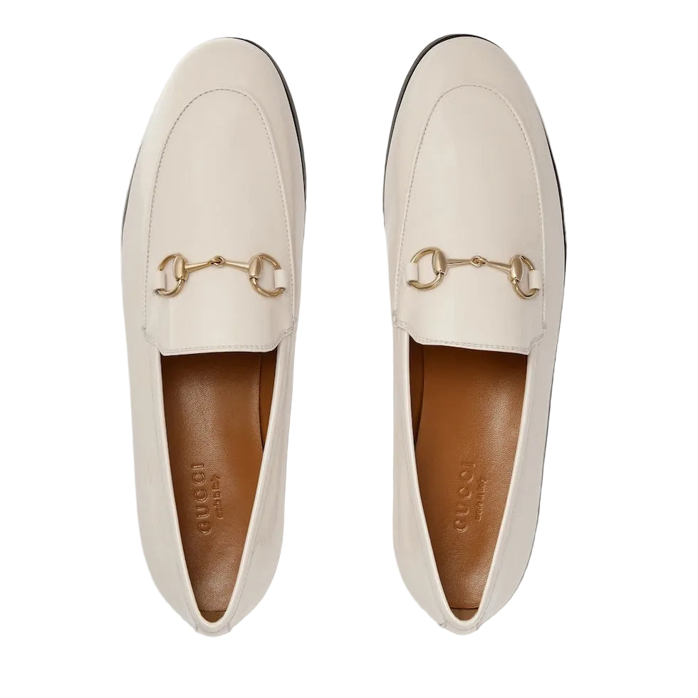 Pair of cream loafers with gold hardware on a light gray background