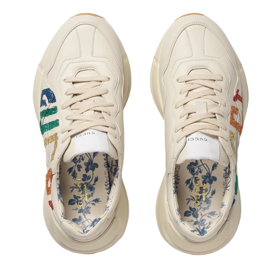 Pair of cream sneakers with colorful branding and floral pattern on a light gray background