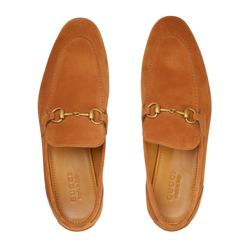 Pair of tan suede loafers with gold buckles on a light gray background