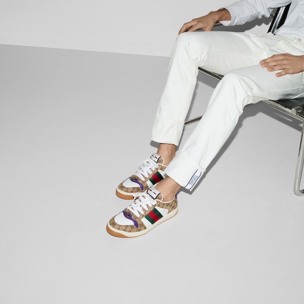 Person wearing colorful sneakers with a brand logo, sitting on a chair against a plain background