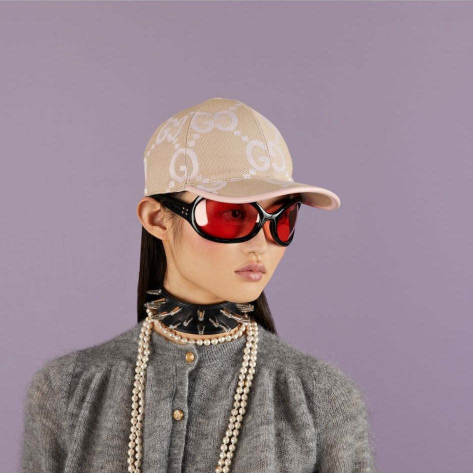 Person wearing a beige cap and red sunglasses on a plain background