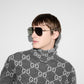 Person wearing a gray sweater with a pattern and sunglasses against a light background