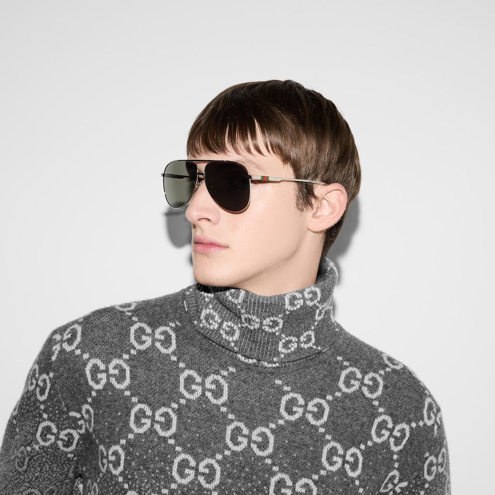 Person wearing a gray sweater with a pattern and sunglasses against a light background