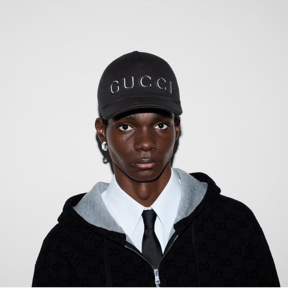 Person wearing a black Gucci cap and black hoodie with white collar on a white background