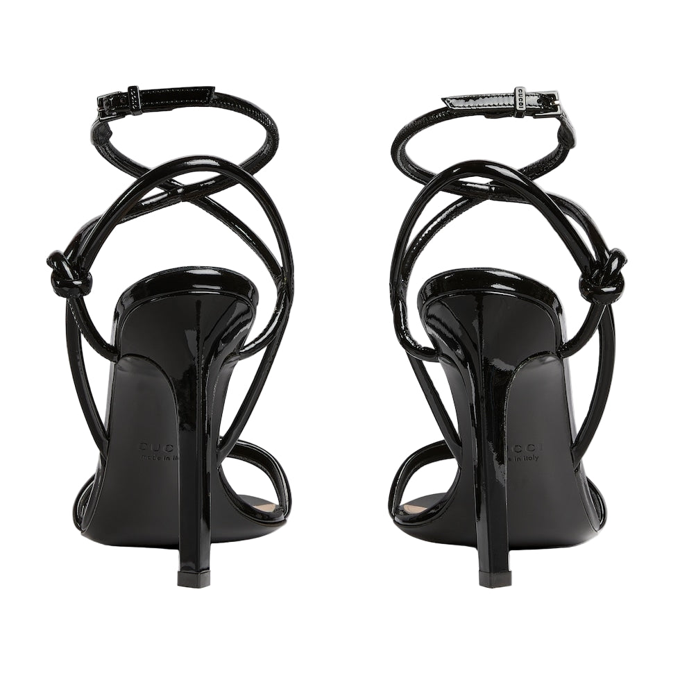 Black high-heeled sandals with strappy design on a light gray background