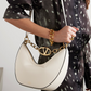 Person holding a white handbag with gold chain detail, wearing a black and white polka dot shirt.
