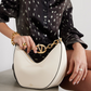 Person holding a white handbag with gold chain detail, wearing a black patterned shirt.