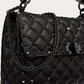 Black quilted handbag with studded details and a chain strap on a light gray background