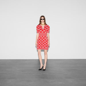 Woman wearing a red patterned dress standing against a plain background