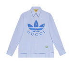 Light blue striped shirt with Gucci and Adidas logos on a light gray background