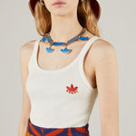 Person wearing a white gucci tank top with Adidas logo and colorful necklace on a plain background