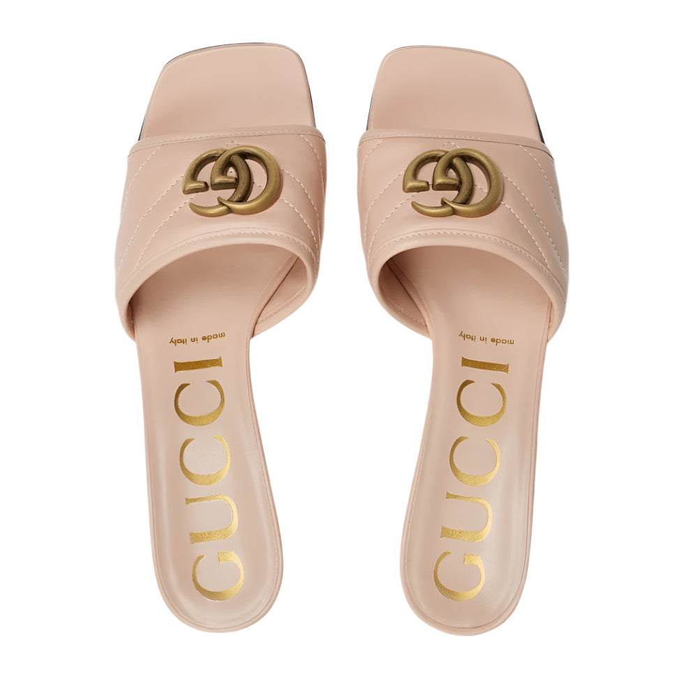 Pair of Gucci slides with gold logo and text on a light gray background