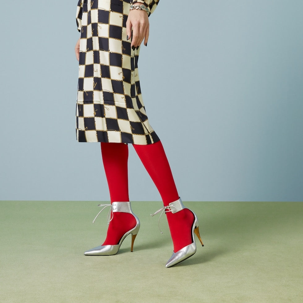 Person wearing a checkered coat, red tights, and red high-heeled shoes on a light gray background