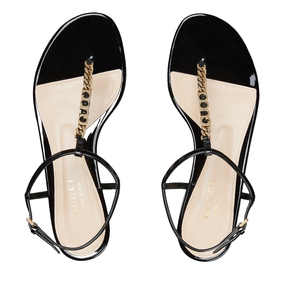 Black sandals with gold straps on a light gray background