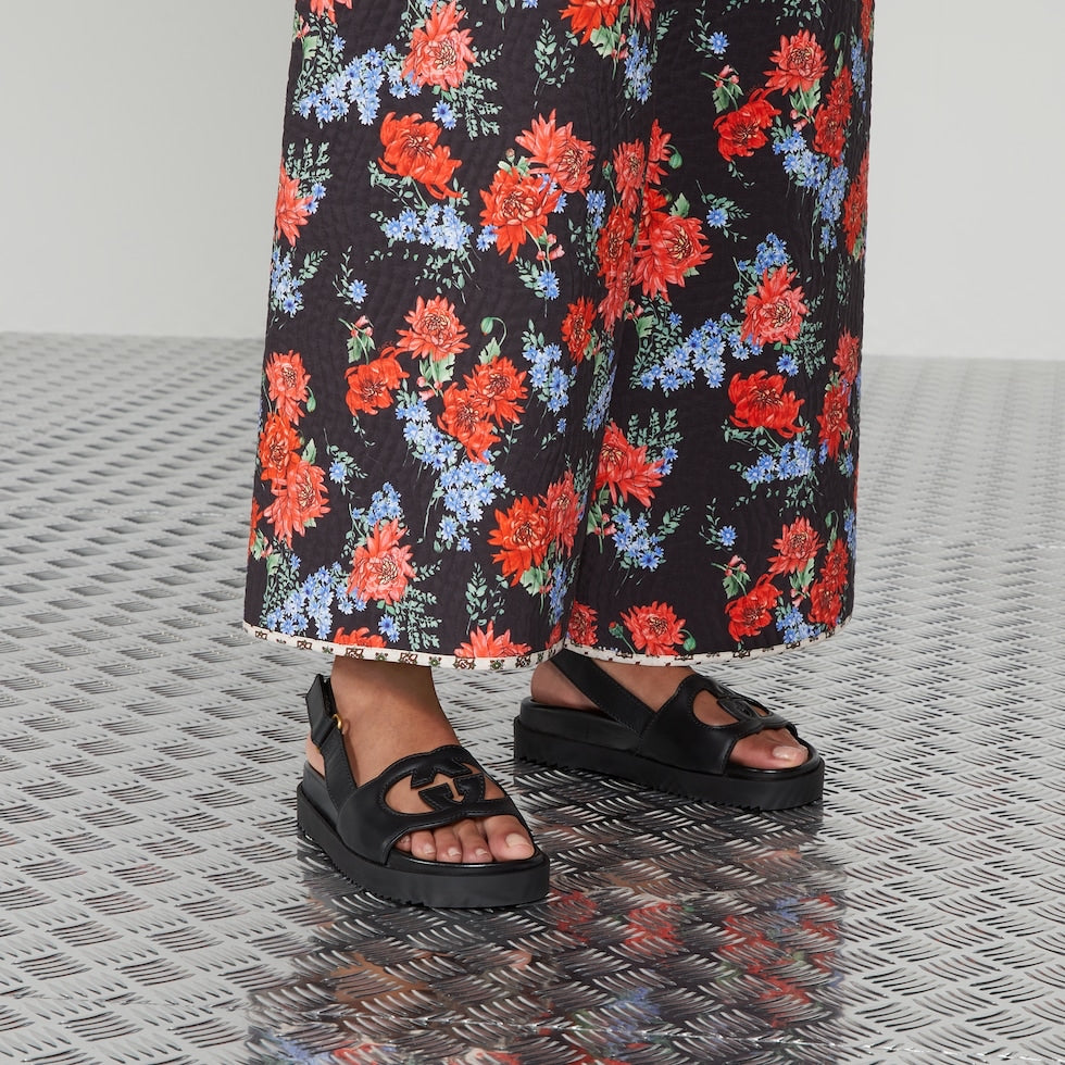 Person wearing black sandals and floral pants on a textured floor.