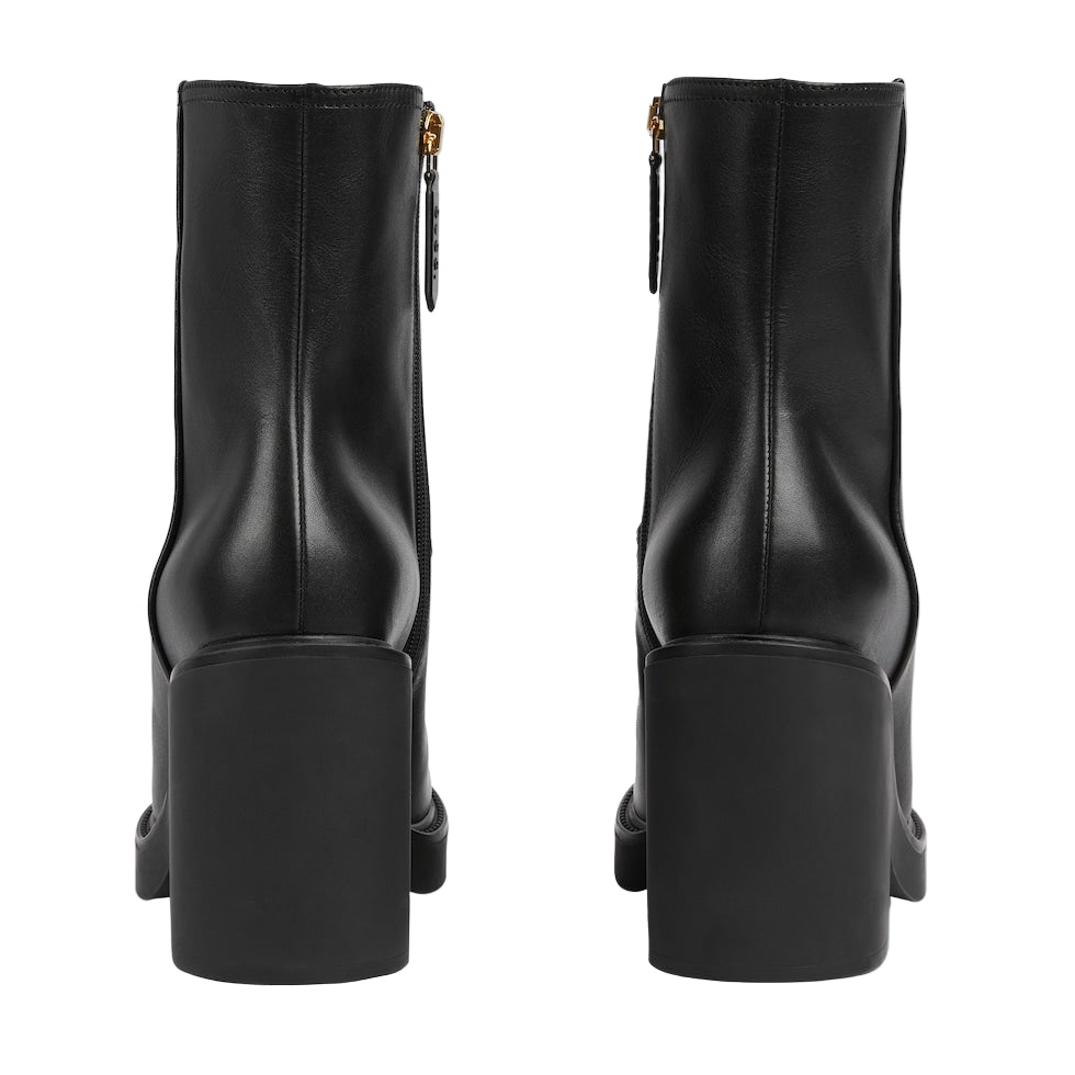 Black ankle boots with gold zipper on a light gray background